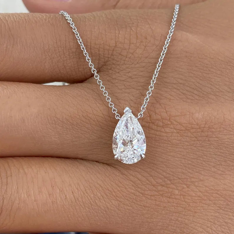 Teardrop-shaped diamond pendant on a chain held between fingers
