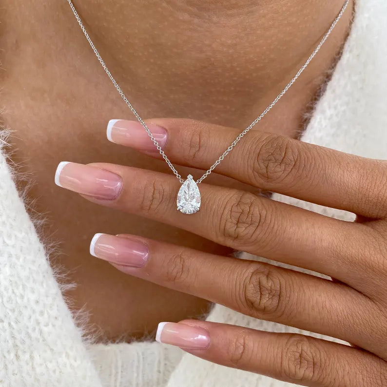 Teardrop-shaped diamond necklace on a hand with a blurred background